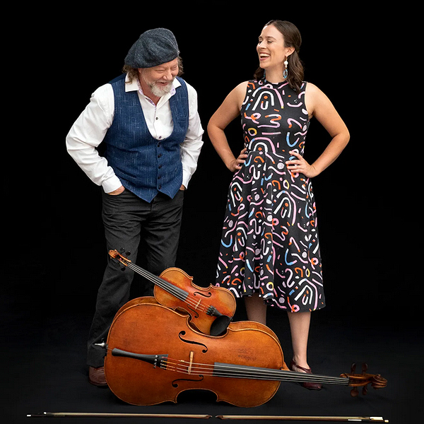 Alasdair Fraser & Natalie Haas laughing together, fiddle and cello stacked at their feet