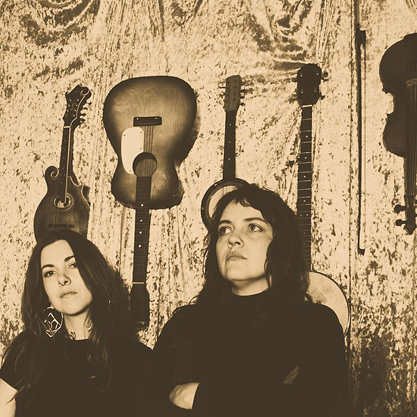 Mama's Broke: two young women with stringed instruments hanging on a wall behind them