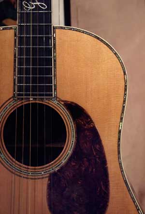 Closeup of a Gibson guitar, showing mother-of-pearl banding around the edge of the instrument, around the soundhole, and around where the fretboard is attached to the top