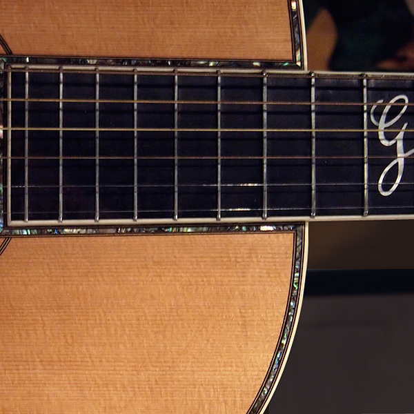Closeup of a Gibson guitar, showing mother-of-pearl banding around the edge of the instrument, around the soundhole, and around where the fretboard is attached to the top