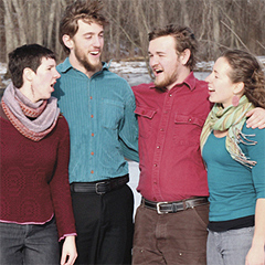 The four young singers of Windborne stand with their arms around one another, singing
