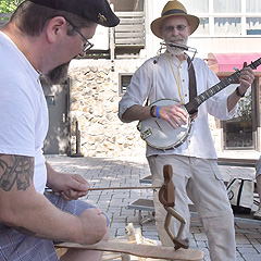 A man makes a limberjack dance while another plays banjo