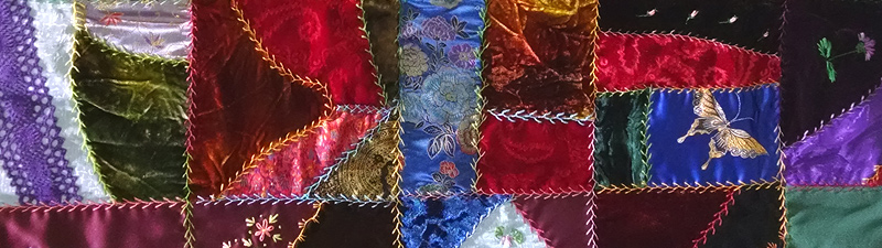A section of a hand-made crazy quilt, made of random-shaped pieces of velvet and satin with embroidered seams and small embroidered motifs such as flowers and butterflies.