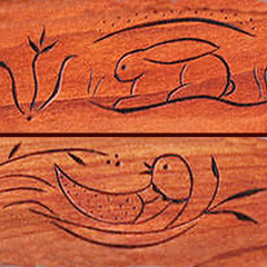 Closeup of two pieces of cherry wood with a simple line carvings in the Pennsylvania Deutsch folk art style: a rabbit in its den and a bird in its nest. The bird is looking back over its shoulder with its beak open.  It looks cheerful. The rabbit is crouched with its ears folded down over its back. Above and below the rabbit are curved lines suggesting the floor and roof of its den. It looks peaceful.