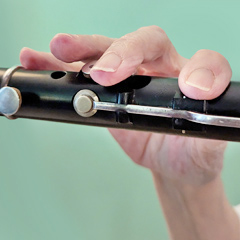 A close-up of Lesl’s right hand as she plays the flute. Her index finger is closing one tone-hole; middle and ring fingers hover over the other two holes.  Her pinky finger rests against the flute.