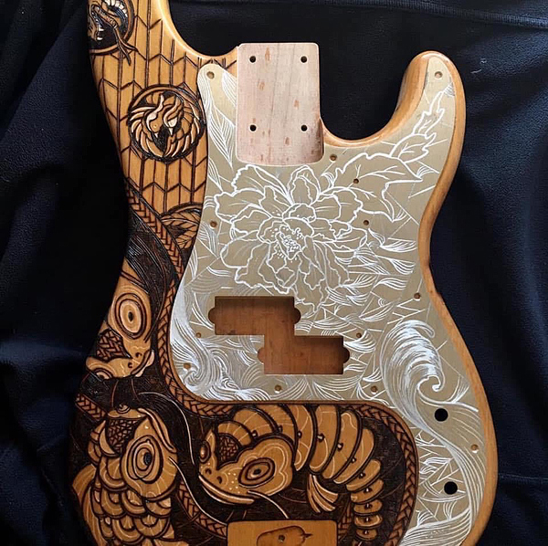 An elaborately decorated electric guitar body. The wooden part is decorated (with wood-burning) with black outlines of Asian-inspired koi fish. The tan plastic pick-guard part is etched (in white) with outlines of flowers and waves.