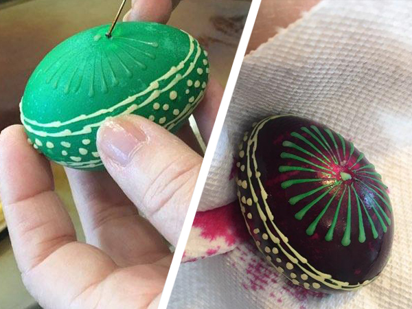 On the right side of this image, we see the completed multicolored egg: it is very dark purple/black, with a green pinwheel design and a band of dots and lines that circles the egg vertically.  On the left, we see the same egg in mid-process: it has been dyed green, and there’s wax over the belt pattern. Barbara is creating the pinwheel pattern by applying wax on the empty face of the egg.