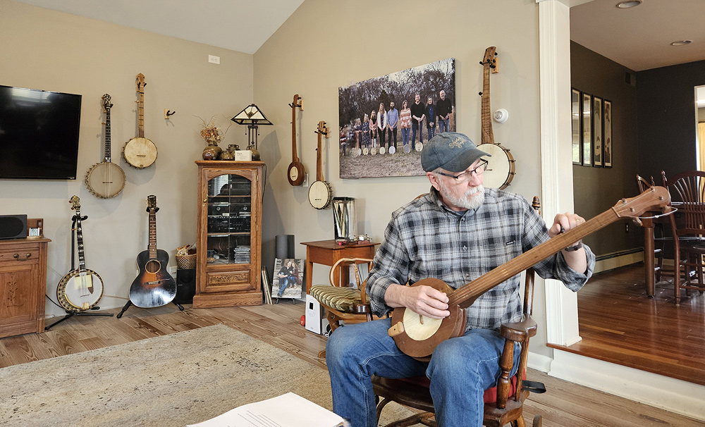 Glenn Carson sits in his living room, tuning the short string of a fretless banjo.