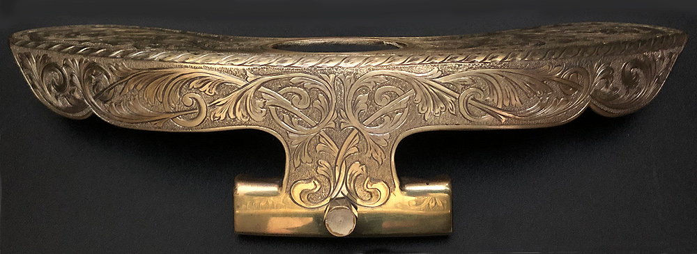 This banjo armrest is made of polished brass with elaborate engravings. It extends 8-10 inches around the banjo's circumference, an inch or two across the skin head, and an inch or so down the outer ring.