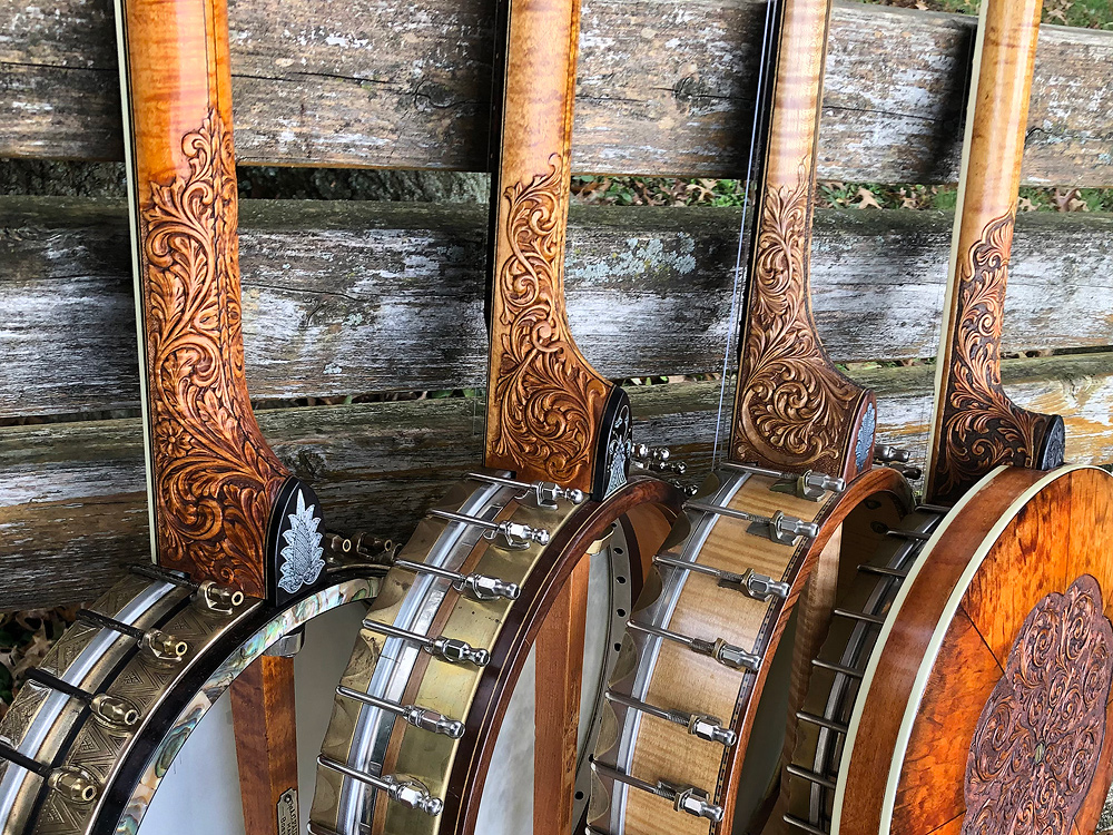 Elaborately carved heels on four banjos made by Glenn, leaned against a weathered wood fence.