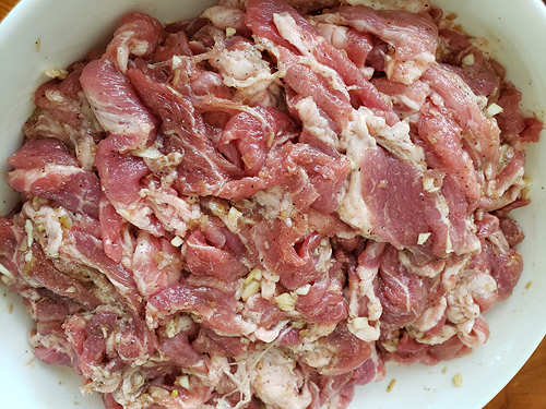 The strips of raw pork are heaped in a white bowl, ready for the next step