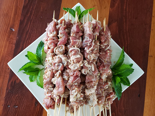 The marinated pork strips have been threaded zigzag-wise onto skewers.  More than a dozen of these, each with several inches of meat on the skewer, are stacked diagonally on a square white plate, with mint sprigs placed artfully on the empty corners.