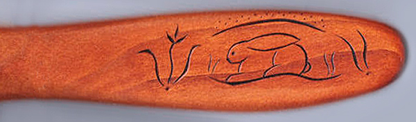 A closeup of a spatula handle decorated with a rabbit crouched in a den.