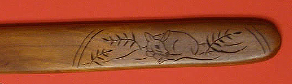 A closeup of a spatula handle decorated with a deer curled up in a bed of ferns.