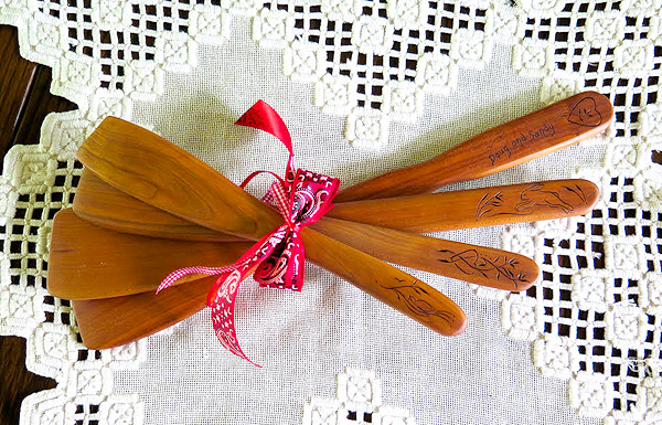 Four small spatulas of different sizes are bundled together with red ribbon. Each handle has a design carved into it: a heart, a running rabbit, wildflowers.