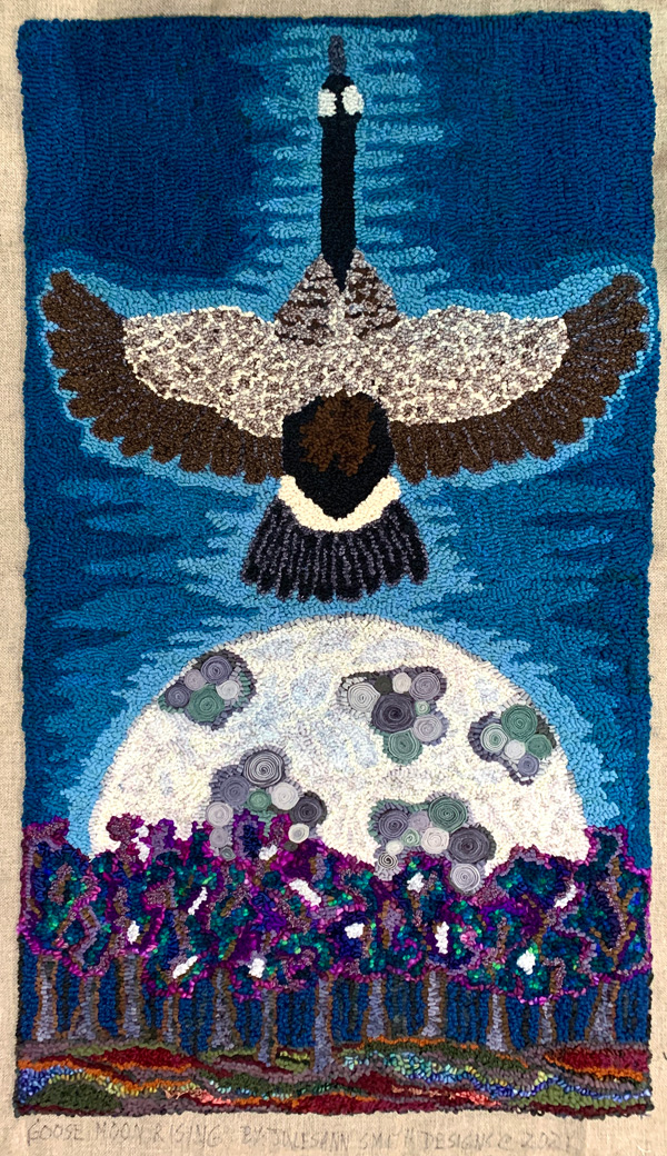 Goose Moon Rising shows a Canada goose in flight, seen from the top with outstretched neck reaching up to the top of the rug and wings stretching out to both side edges. Below the goose is a huge grayish-white moon rising from a line of trees done in jewel tones of purple, teal and blue. The moon has ‘craters’ of darker gray and green. The goose’s back, wings and tail are shaded and detailed with appropriate colors.  The background is an evening sky, light blue near the goose and fading to darker blue near the edges of the rug. The finished rug appears to be about two feet wide and four feet tall.