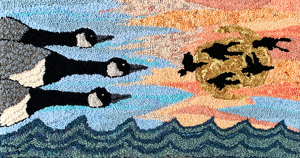 This hooked rug, which appears to be about 3 feet high by 5 feet wide, shows Canada geese in flight over water.  At left are three geese: their shoulders are just entering the frame and their heads are about a third of the way across the rug, against sky done in various shades of blue. These geese are the focal point and they dominate the left half of the design.  Centered in the right half are five much smaller geese, also flying from left to right, all black, silhouetted against a golden sun and wispy clouds in shades of peach. At the bottom are rows of scalloped waves in shades of dark teal and greenish-gray.