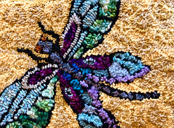 A colorful dragonfly, done in jewel tones of purple and blue, outlined in black, set off by a shaded background of gold and tan.