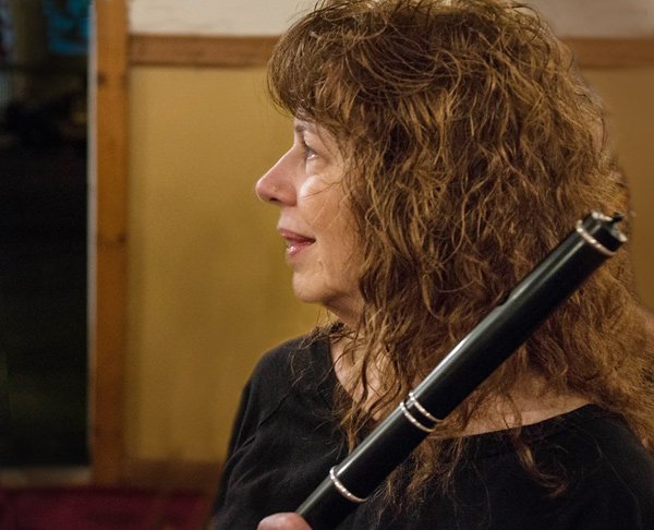 Lesl Harker in profile, watching someone. She holds her flute at an angle; only the top several inches are visible in the photo. She has a mass of wavy auburn hair.