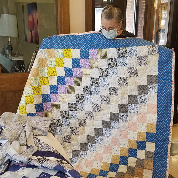 Sharon holds a quilt made of long diagonal rows of blocks, pieced so that squares of each color meet only at opposite corners.  Some prints appear in more than one row; others appear in only one row.