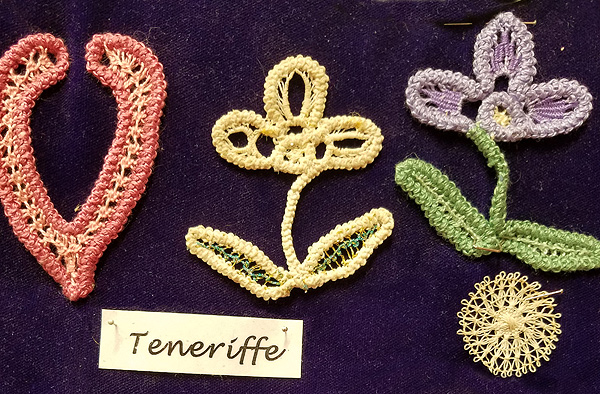 Three pieces of teneriffe lace, made with colored thread.  Two are 3-petal flowers with leaves; one is an outline suggesting a heart shape, with an open top.