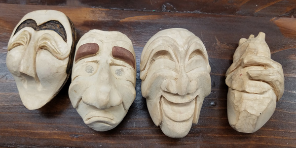 Three stylized facial carvings of Talchum characters. Two of the three have heavy eyebrows stained black or brown. To the right of those three is an anatomically correct carving of a human heart, about the same size as the faces.