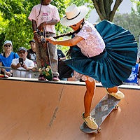 A portion of a photo showing a member of ImillaSkate riding her skateboard. She is coming down the side of a steep ramp, having just turned 180 degrees, and her blue skirt and lace under-skirt are swirled out perpendicular to her body.